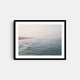 A framed fine art photography print featuring the blue ocean coastline and surfers in Manhattan Beach, California.