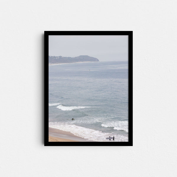 A framed fine art photography print featuring a single surfer in light blue ocean waters in Malibu, California.