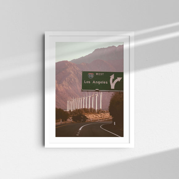 A framed fine art photography print featuring wind mills and a highway sign for Los Angeles in Palm Springs, California.